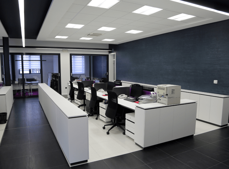 blue greyish office with white desktops and square lights on the ceiling