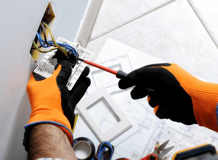worker with orange and black gloves fixing an outlet of a house